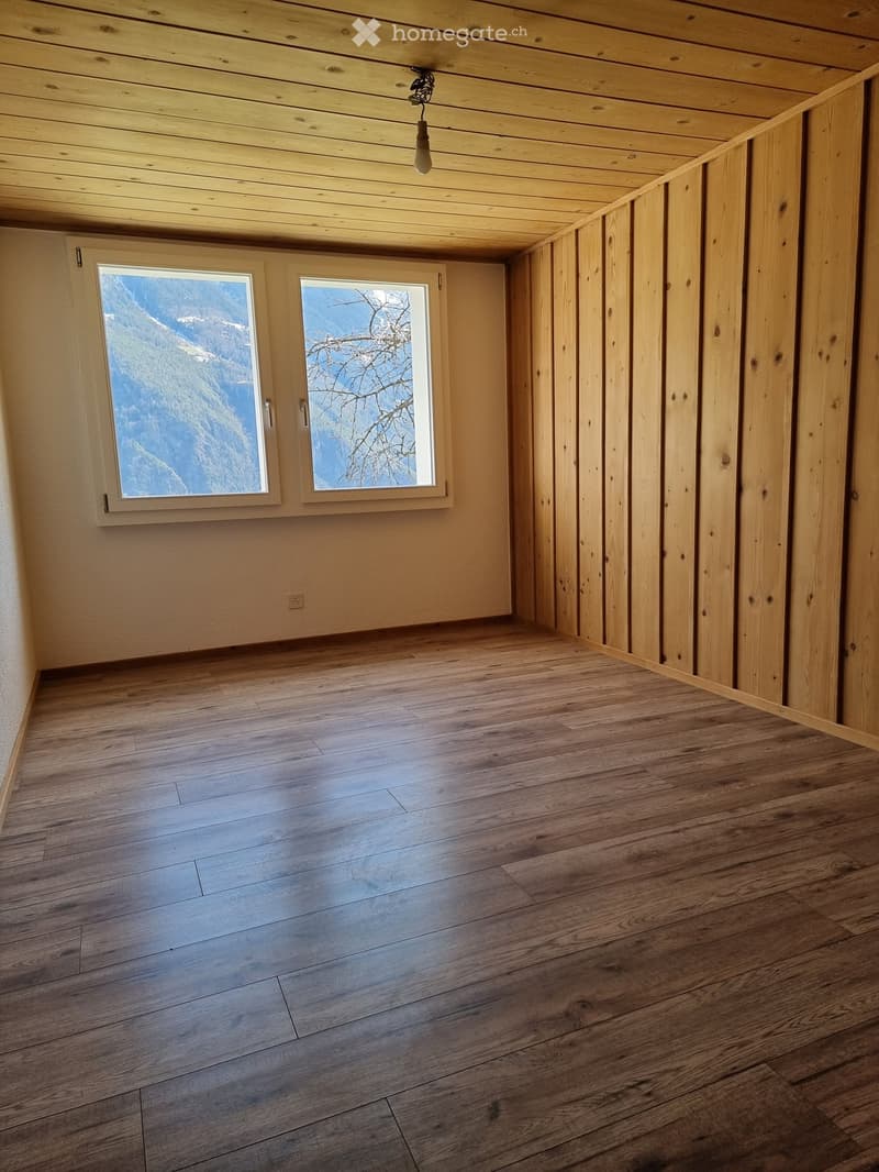Empty room with wooden flooring, wooden ceiling, and large windows offering a scenic mountain view.