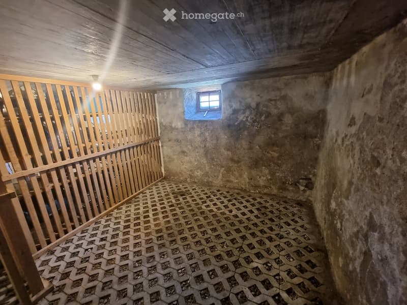 Empty room with exposed wooden ceiling, concrete walls, and a patterned tile floor. A small window is visible on one wall, and a wooden railing is present on the left side.