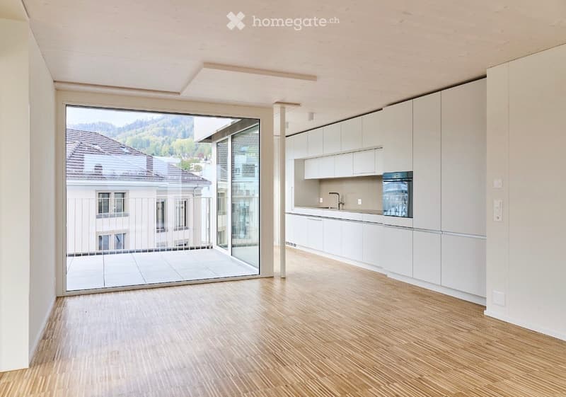 Modern kitchen with white cabinets, wooden flooring, and a large sliding glass door leading to a balcony with a scenic view.