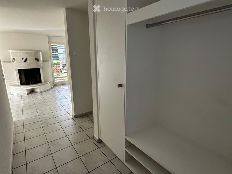 Hallway with tiled floor, white walls, fireplace on left, closet on right, and a door leading to a balcony.