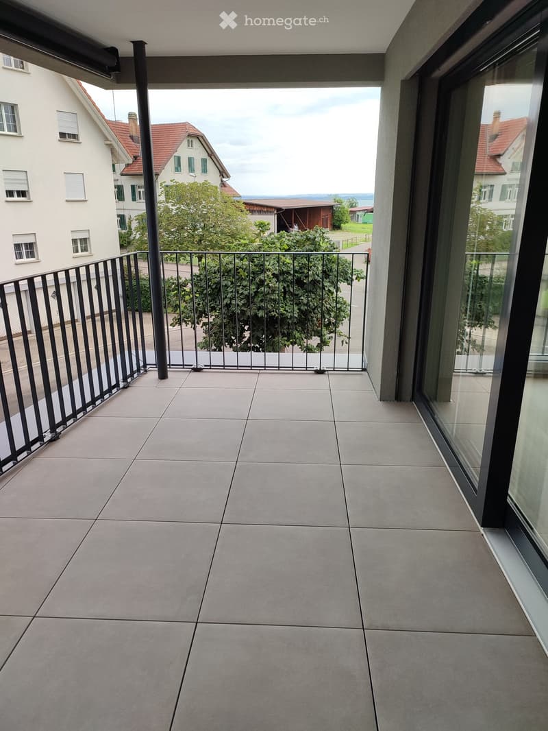 Balcony with tiled floor, metal railing, and view of neighboring houses and greenery.