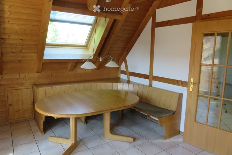 Cozy attic room with wooden walls, a round wooden table, built-in bench seating, pendant lights, and a skylight window.