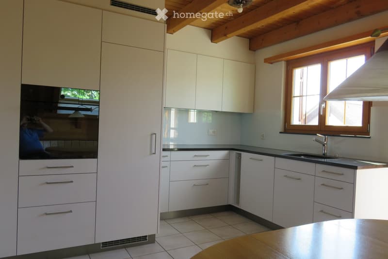Modern kitchen with white cabinets, stainless steel sink, and wooden ceiling beams. Features include a built-in oven and ample storage space.