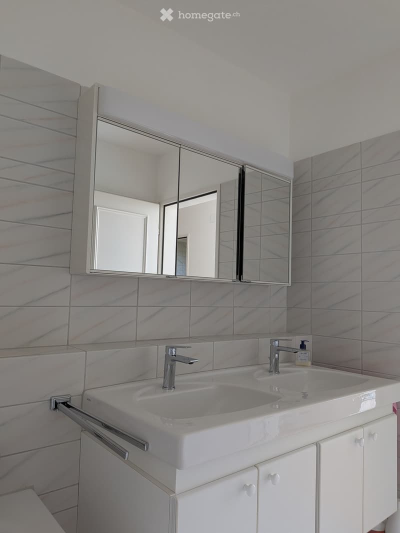 Modern bathroom with a double sink, sleek chrome faucets, a large mirrored cabinet, and marble tiled walls.