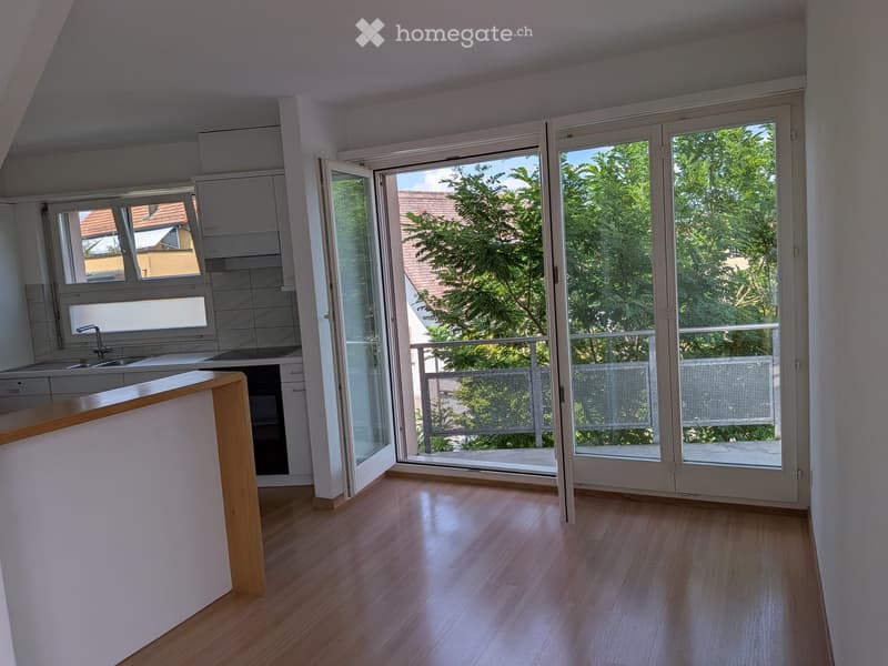 Bright, modern kitchen with wooden flooring, white cabinets, and a kitchen counter. Large sliding glass doors open to a balcony with a view of greenery.
