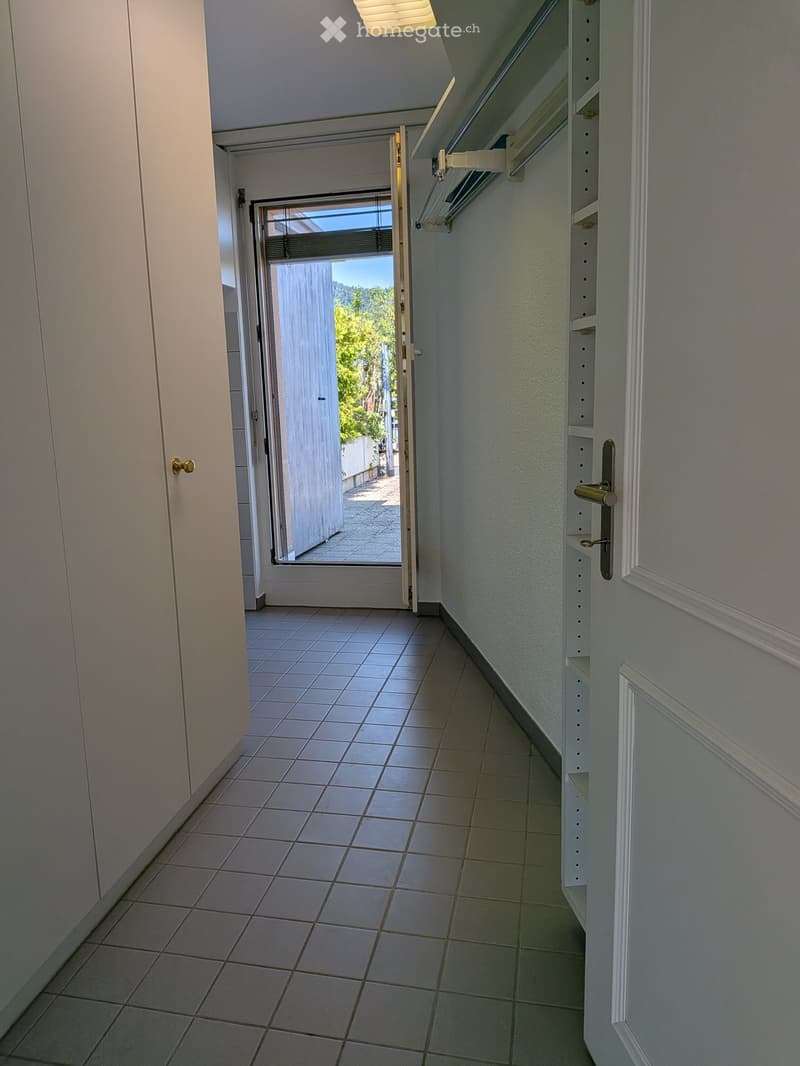 Empty hallway with tiled floor, white walls, and an open door leading to an outdoor area.