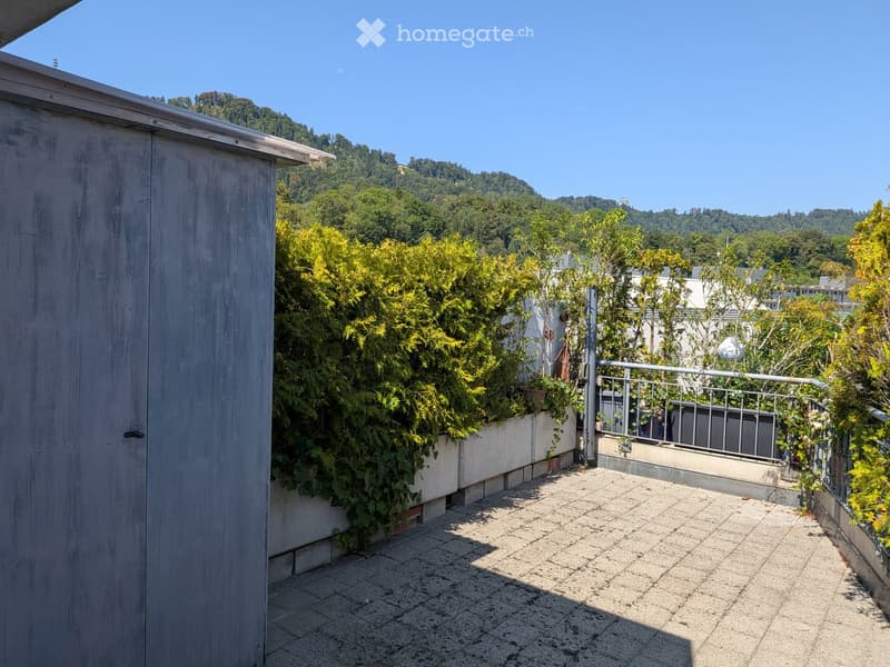 Terrace with tiled floor, metal railing, and lush greenery, overlooking a scenic hillside.