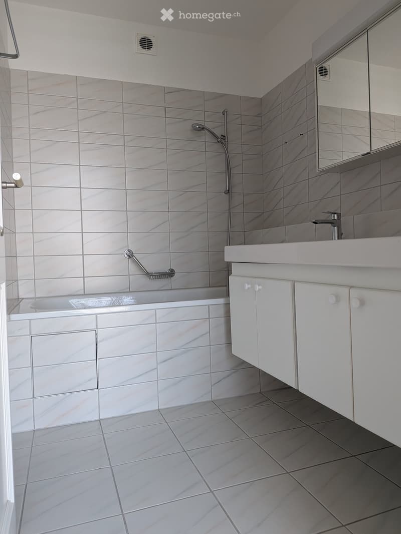 Modern bathroom with white tiled walls and floor, featuring a bathtub, sink, and mirrored cabinet.