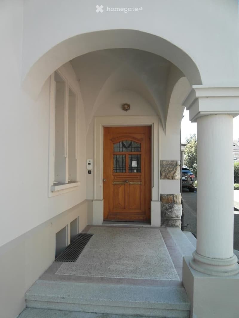 Entrance to a building featuring a raised ground floor, stone steps, and a wooden double door with glass panels.