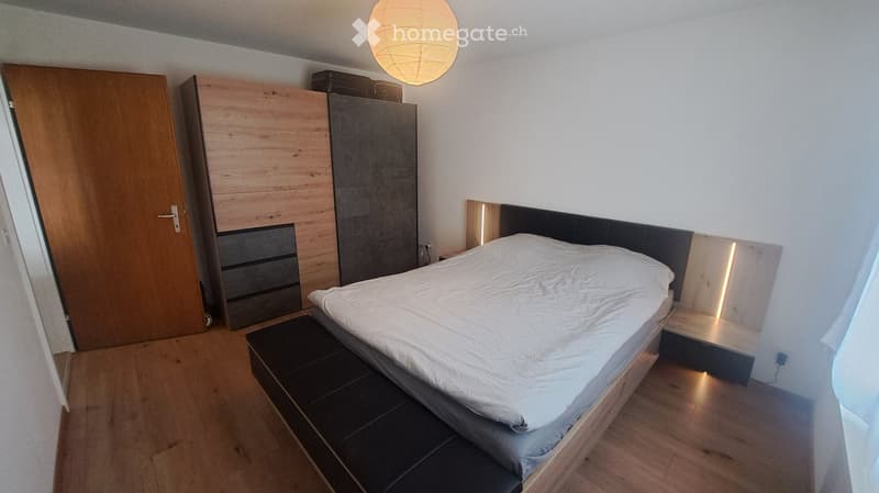 Modern bedroom with a wooden bed, white bedding, built-in wardrobe, and a hanging spherical lamp.