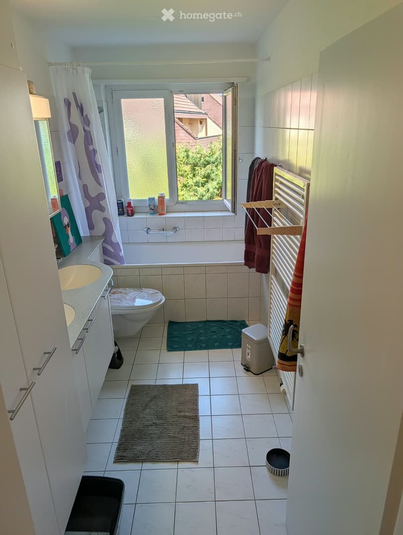 Bathroom with a sink, toilet, bathtub, towel rack, towels, rugs, and a window with a view of the garden.