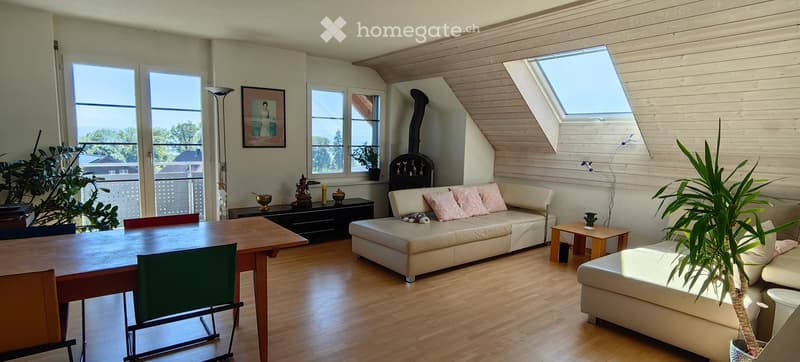 Bright living room with wooden floors, large windows, a white leather sofa, ottoman, dining table, chairs, floor lamp, and fireplace.