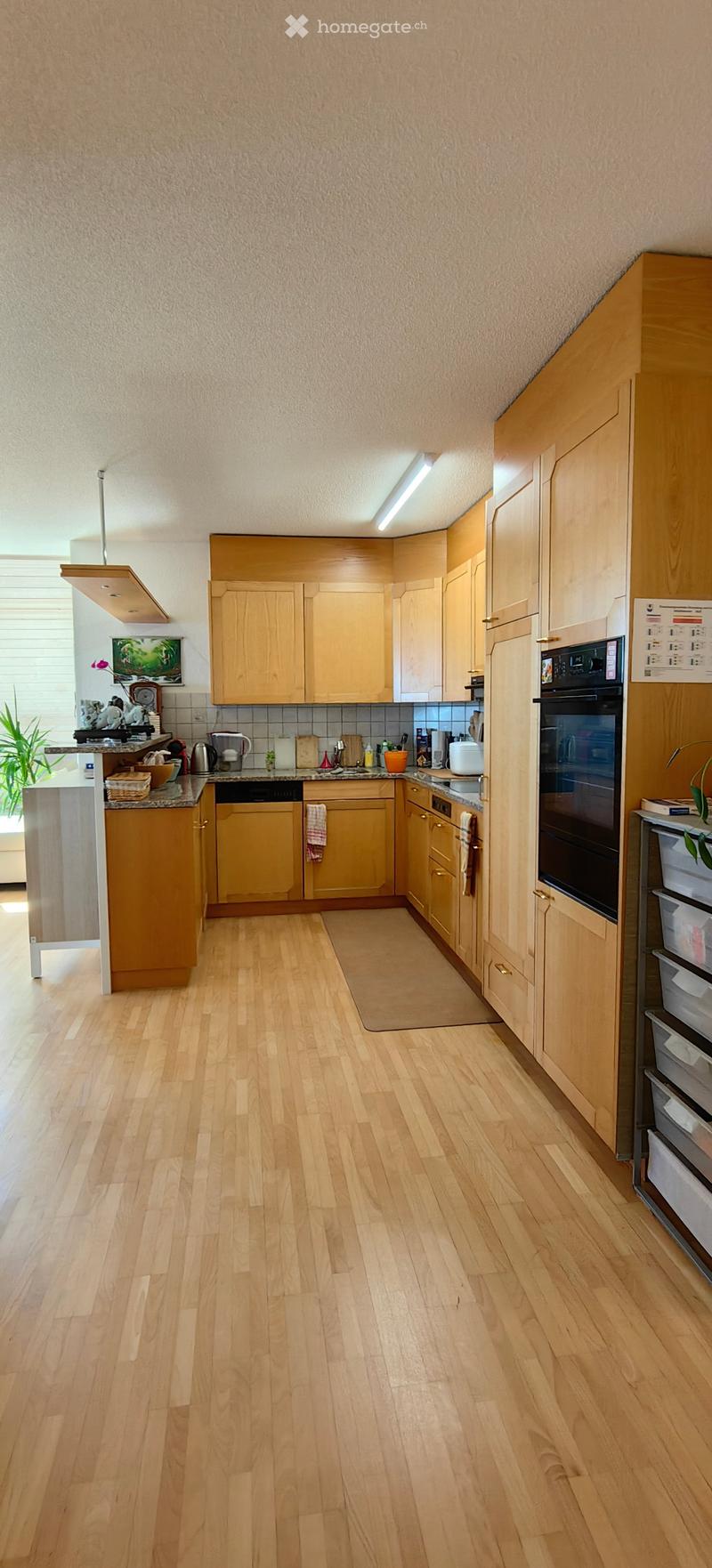 Bright kitchen with light wooden cabinets, stainless steel appliances, and a central island. The floor is light wood, and the walls are painted in a neutral tone.