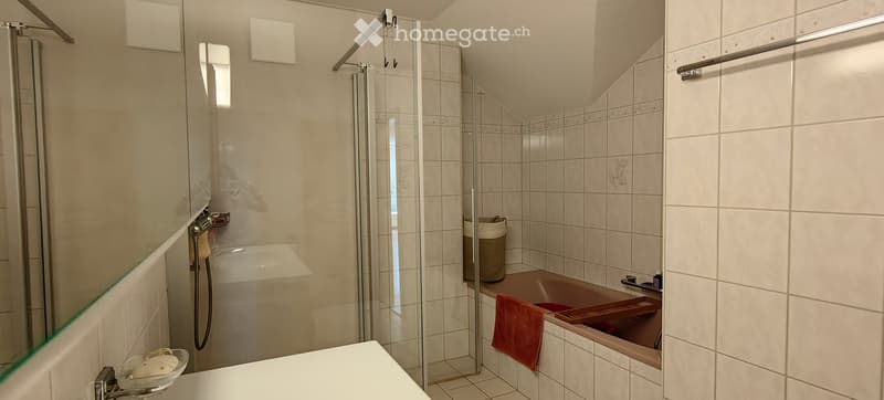 Modern bathroom with a bathtub, glass-enclosed shower, tiled walls, and a towel on the edge of the tub.