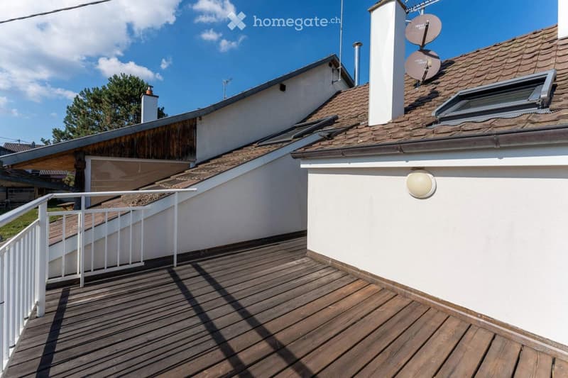 Wooden deck with white railing, adjacent to a white building with a tiled roof and satellite dishes.