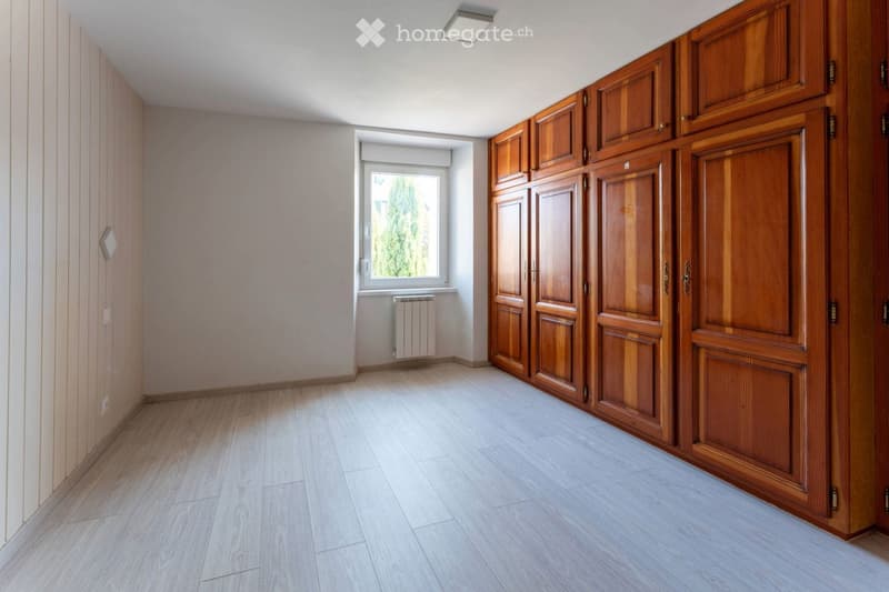 Empty hallway with wooden doors, light-colored walls, and a window with a radiator below it.