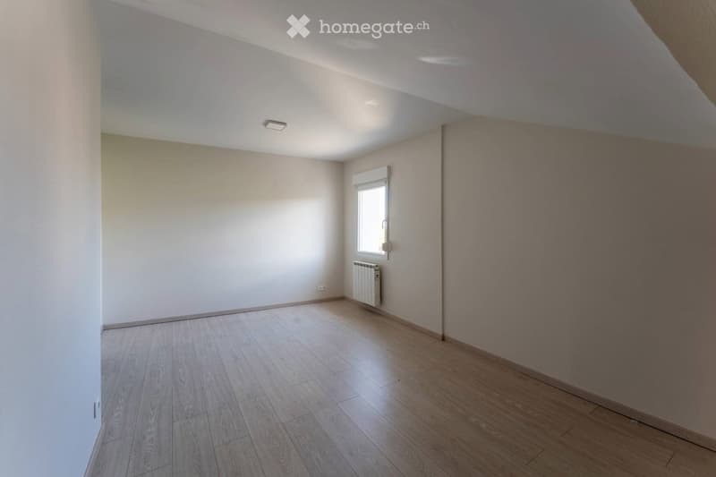 Empty room with wooden flooring, white walls, and a single window with a radiator below it. The ceiling has recessed lighting.