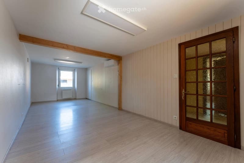 Empty hallway with wooden flooring, white walls, and a wooden door with glass panels leading to another room.