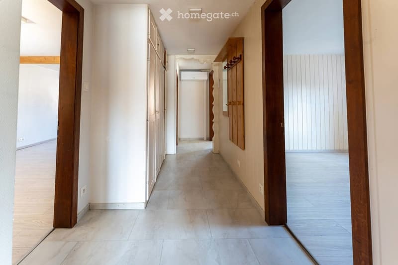 Clean, well-lit hallway with tiled flooring, white walls, wooden doors, and built-in wooden cabinetry on one side.