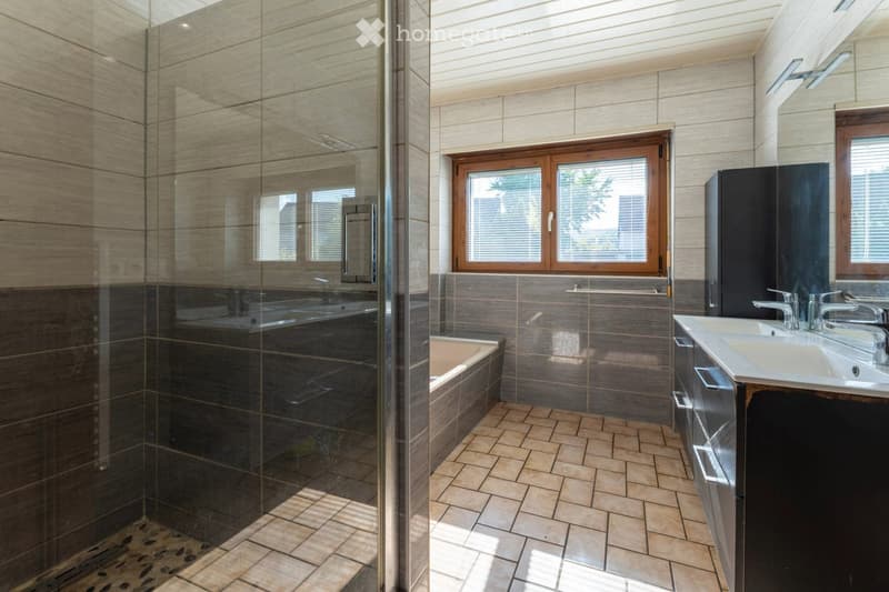 Modern bathroom with a glass-enclosed shower, bathtub, double sink vanity, and large windows providing natural light.