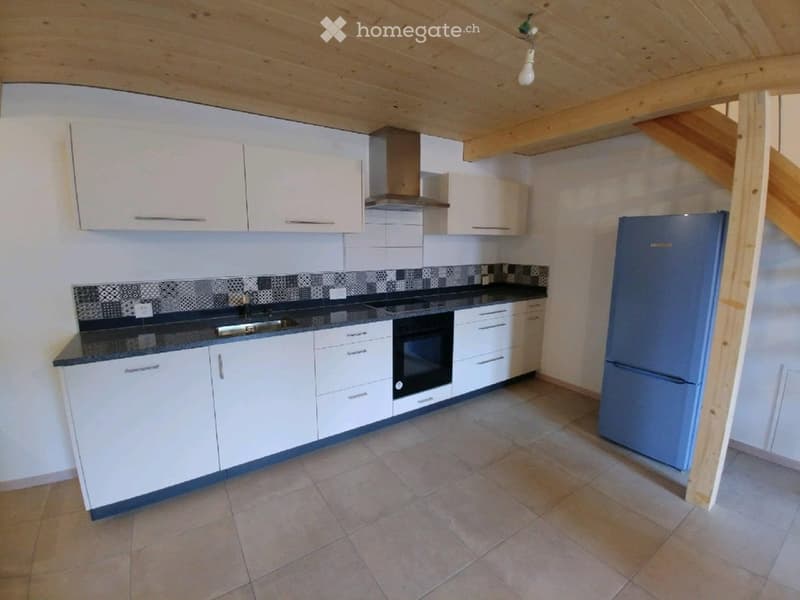Modern kitchen with white cabinets, a blue refrigerator, a black countertop, and a tiled backsplash. The space features a wooden ceiling and tiled flooring.