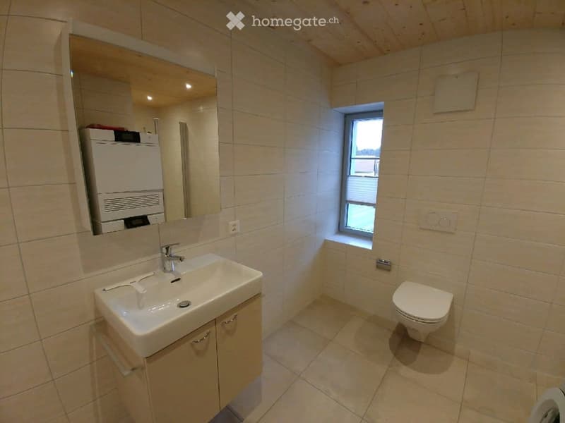 Modern bathroom with beige tiles, a white sink with a modern faucet, a large mirror, a toilet, and a small window providing natural light.