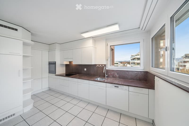 Modern kitchen with white cabinets, stainless steel appliances, and a dark brown countertop. Features a large window with a view of the city.