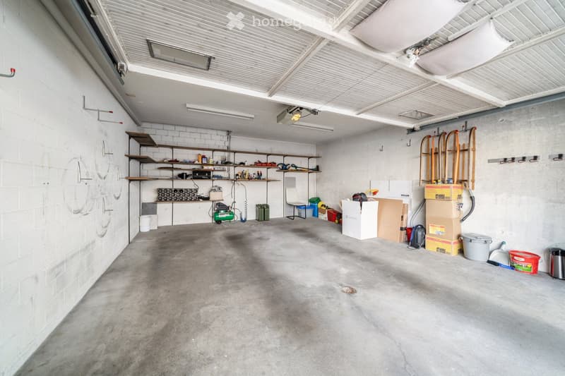 {"type": "Garage", "objects": ["shelves", "tools", "storage boxes", "chair", "green machine", "buckets", "cardboard boxes"], "description": "A spacious garage with concrete flooring, white brick walls, and metal shelving units holding various tools and st