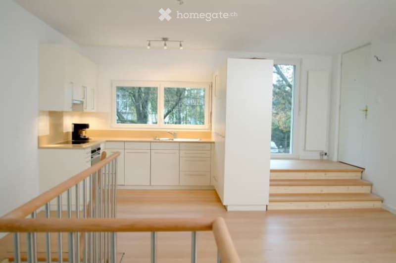 Bright, modern kitchen with white cabinets, a central island, and a staircase leading to another level. The space features a sink, faucet, coffee maker, and dishwasher.
