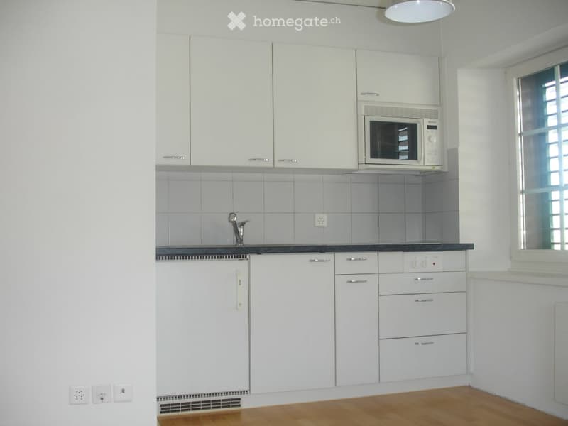 Modern kitchen with white cabinets, a microwave, a faucet, and a refrigerator. The space features light wooden flooring and tiled backsplash.