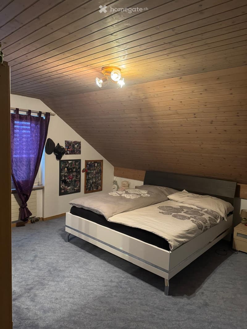 Cozy attic bedroom with wooden slanted ceilings, a large double bed with patterned bedding, nightstand, and decorative wall art.