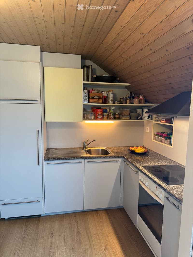 Compact kitchen with white cabinets, stainless steel sink, electric stove, and wooden flooring.