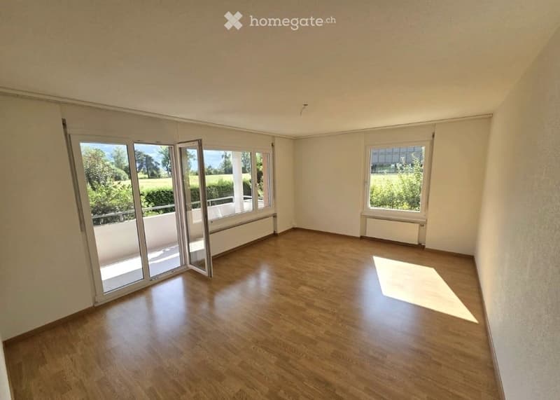 Empty room with wooden flooring, large windows, and sliding glass doors leading to a balcony.