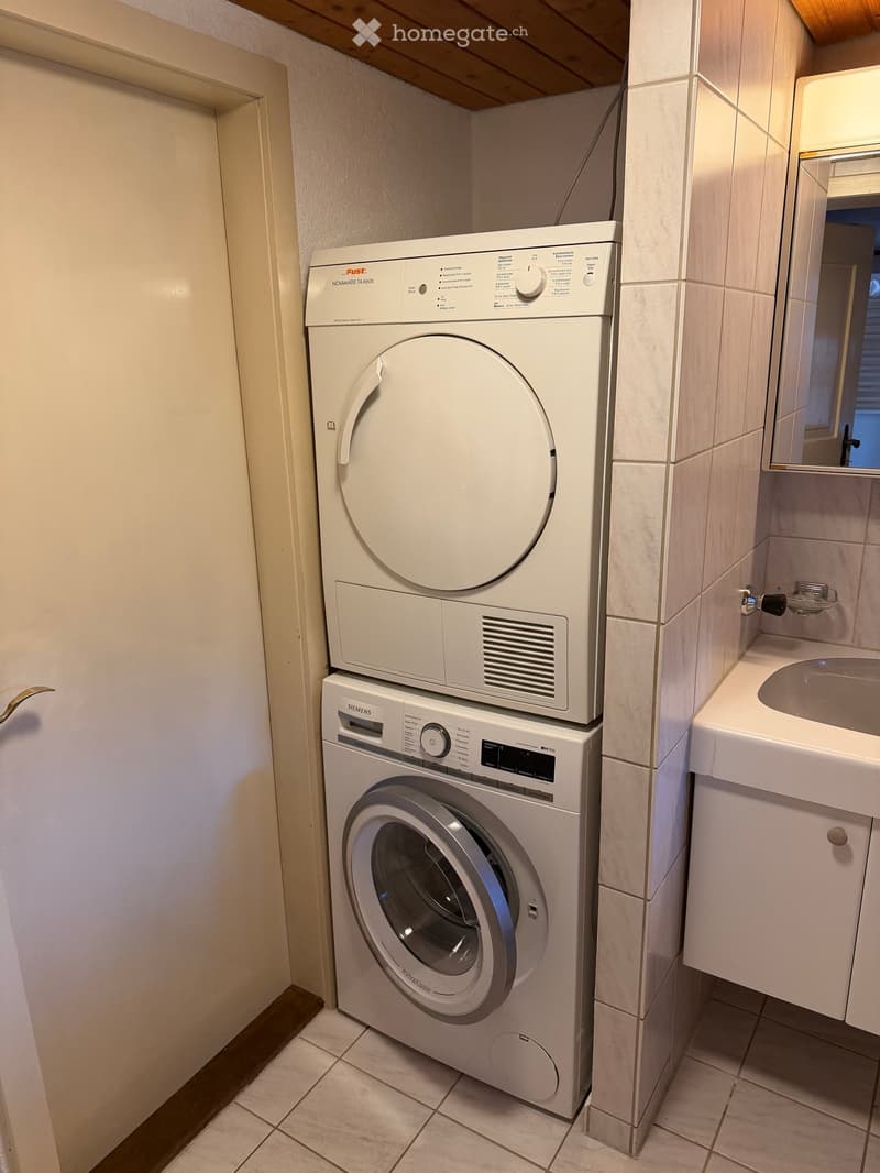 Bathroom with a washing machine and dryer stacked, a sink with a mirror, and tiled walls and floor.