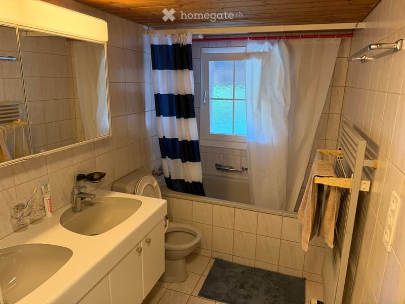 Bathroom with a sink, toilet, bathtub, and shower curtain. Includes a mirror, towel rack, and personal care items on the sink.