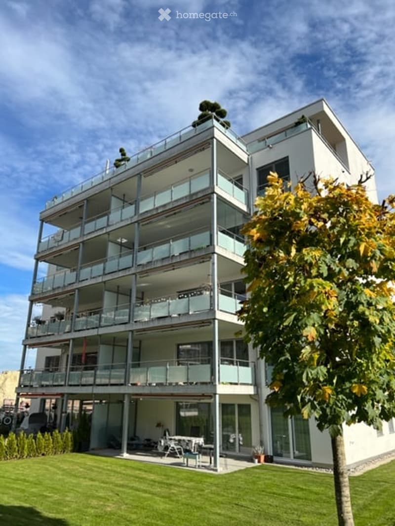 Modern multi-story building with large glass balconies and a well-maintained lawn in front.