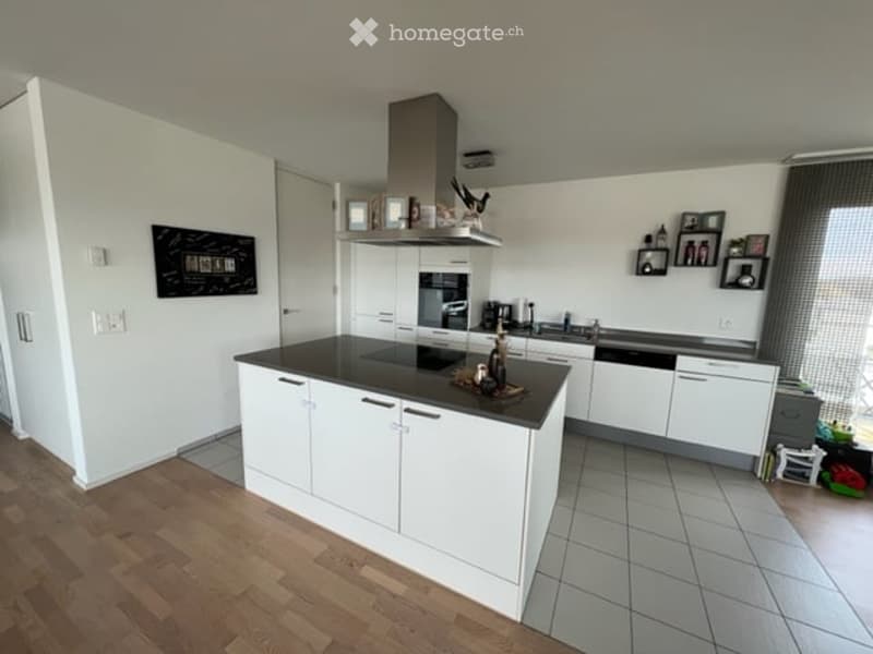 Modern kitchen with white cabinets, black countertop, island, induction cooktop, range hood, oven, dishwasher, and framed pictures on the wall.