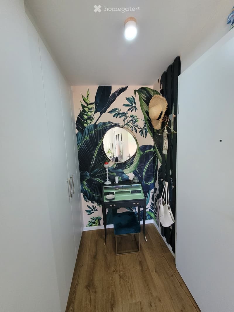 A small, stylish hallway with a wooden floor, a large mirror, a small table with a stool, and a hanging handbag.