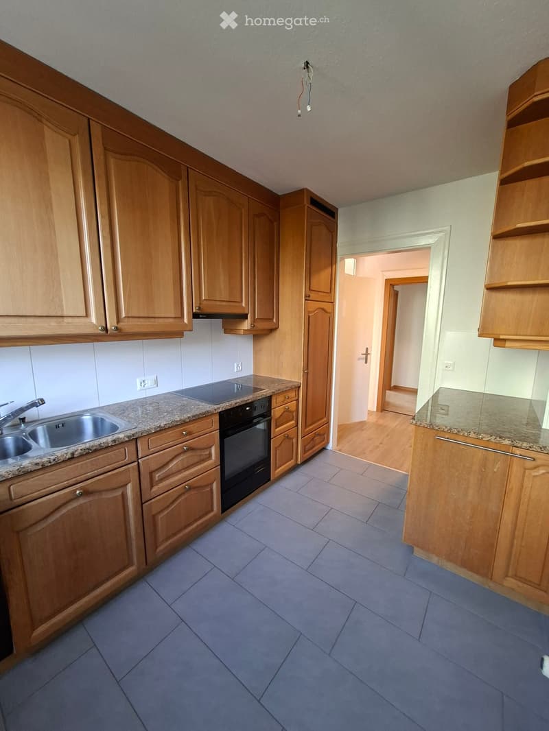 Empty kitchen with wooden cabinets, granite countertops, a sink, and an oven. Blue tiled floor and white walls.