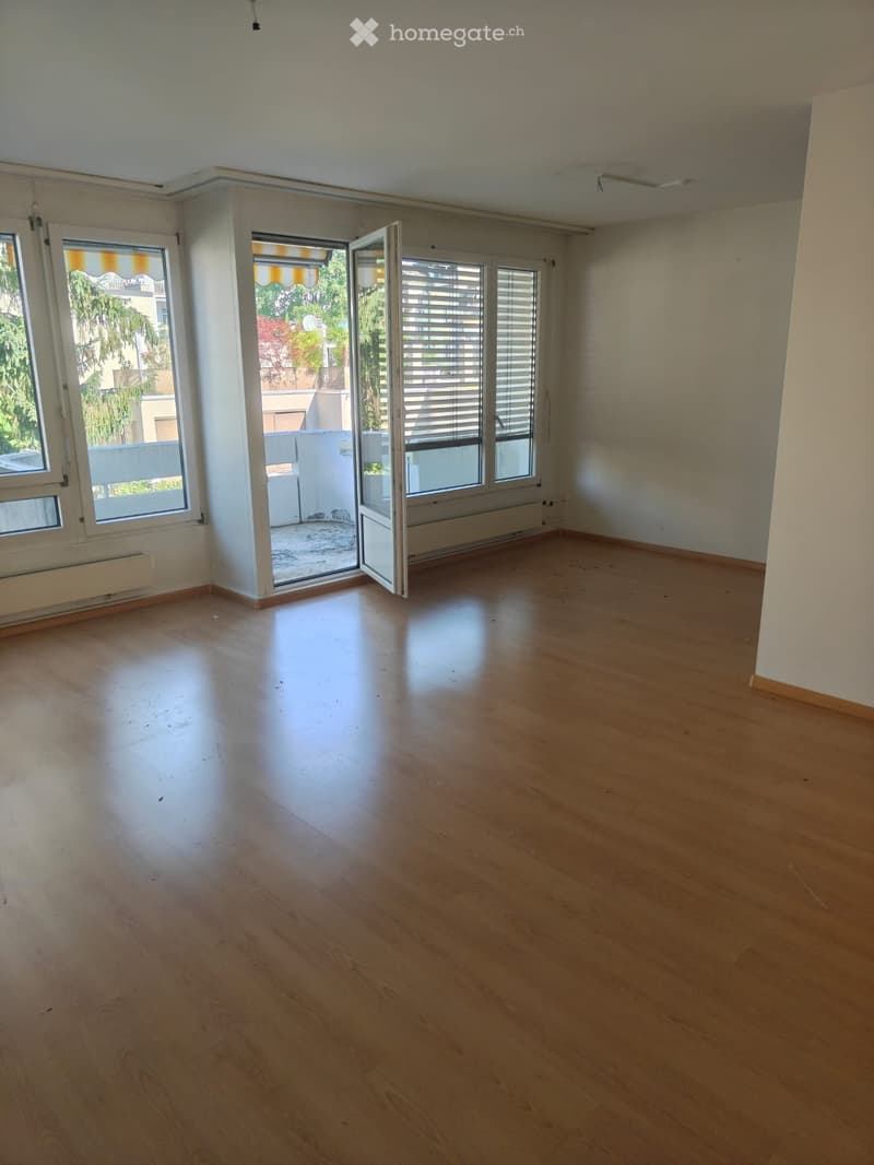 Empty room with wooden flooring, large windows, and an open door leading to a balcony area.