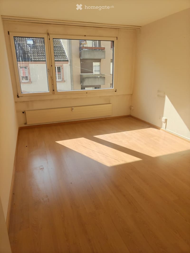 Empty room with wooden flooring, large windows, and radiators on the walls.