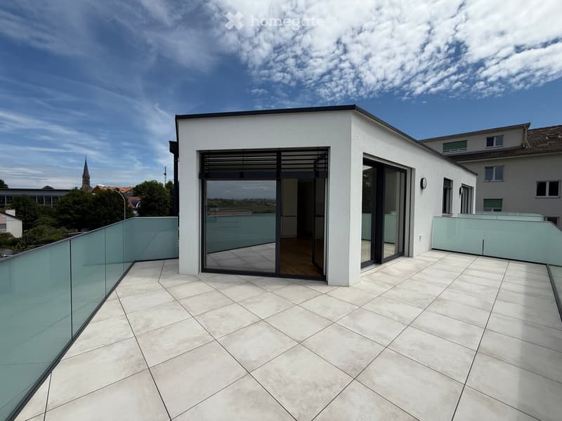 Rooftop with tiled floor, glass railing, and sliding glass doors, leading to an enclosed balcony