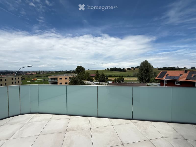 Balcony with glass railing, white tiles, rural landscape, greenery, trees, buildings, cloudy sky