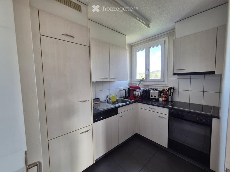 Modern kitchen with white cabinets, black countertops, and stainless steel appliances including an oven, dishwasher, and coffee maker. Features a window with a view, a sink with a faucet, and various small appliances on the counter.