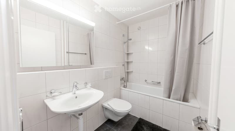 Modern bathroom with white tiles, a sink, toilet, bathtub, and a shower area with a curtain.