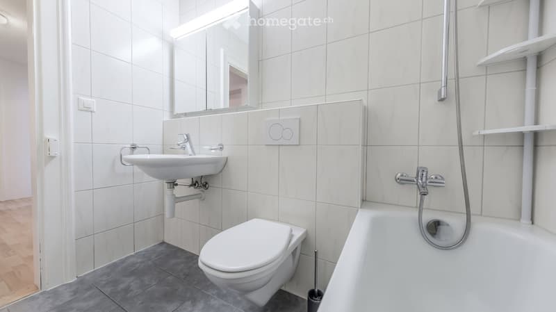 Modern bathroom with white tiles, a sink, toilet, bathtub, and a mirror above the sink.