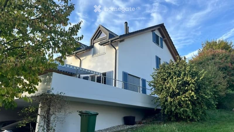 Modern two-story house with white exterior, blue shutters, and a large balcony on the first floor.