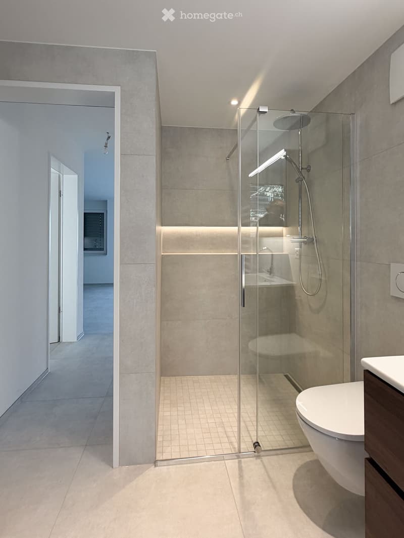 Modern bathroom with a glass-enclosed shower, toilet, and sleek fixtures. The space features light-colored tiles and a clean, contemporary design.