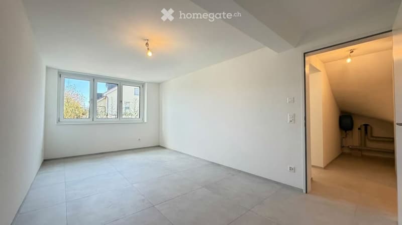Empty room with white walls, tiled floor, and a window with a view of trees. There is a doorway leading to another room with visible pipes and a small black object.