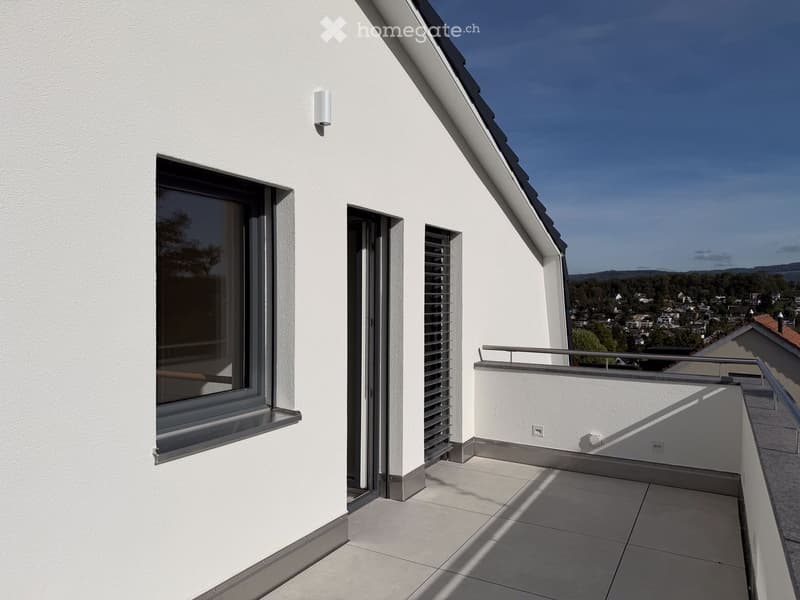 Modern balcony with white walls, large window, sliding glass door, metal railing, and scenic view of town and landscape.